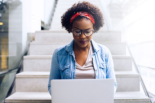 Focused young African student sitting on stairs using a laptop