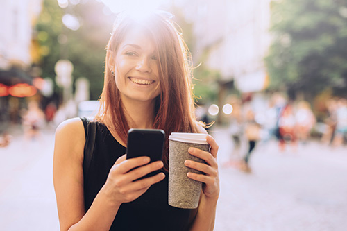 Young woman with smart phone and coffee outdoors