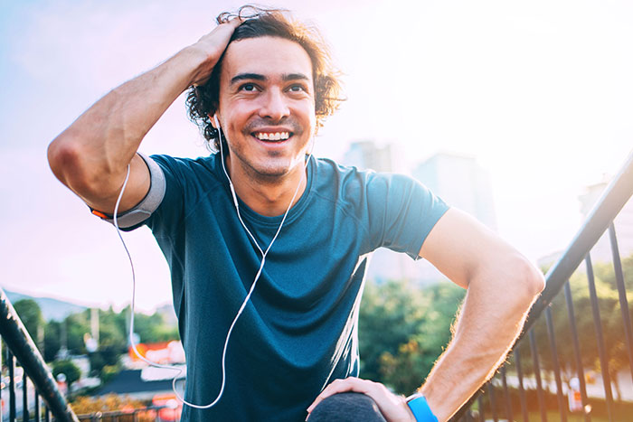 Young man in sports wear exercises at sunlight outdoors in the city