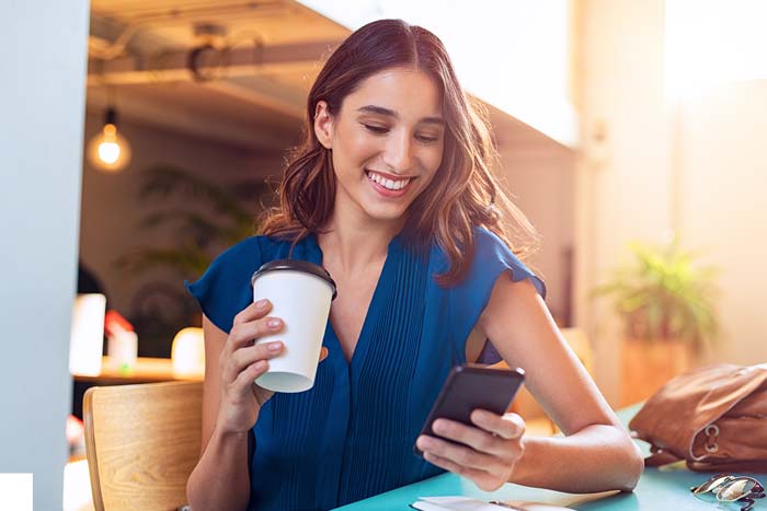 Young beautiful woman holding coffee and looking at smartphone