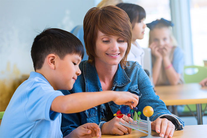 Teacher using solar system model to teach young student