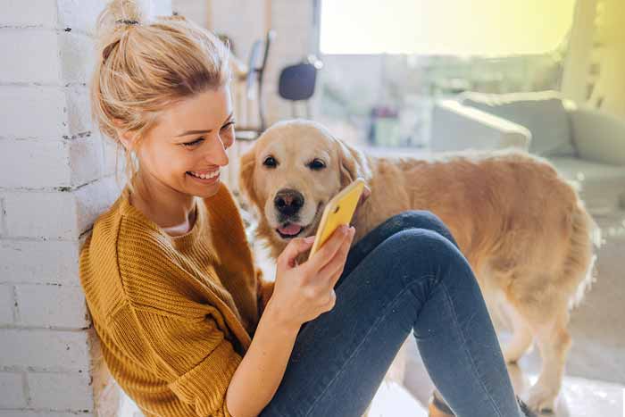 Young woman reading morning news online while her dog standing next to her
