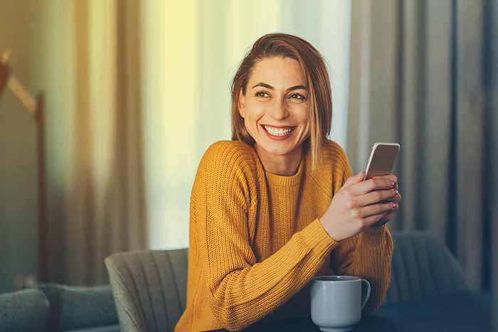 Happy woman at home sitting and texting on the phone