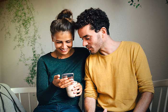 Smiling young couple looking at phone while having coffee