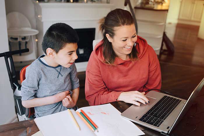Smiling mother showing video to autistic son on laptop at home