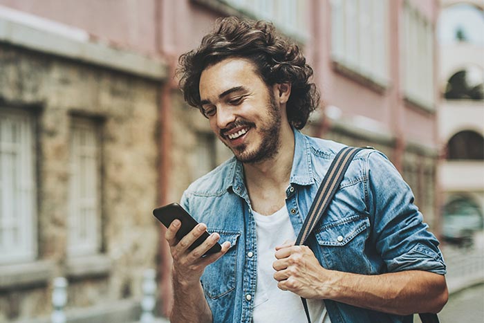 Smiling young man walking outdoors and looking at his phone