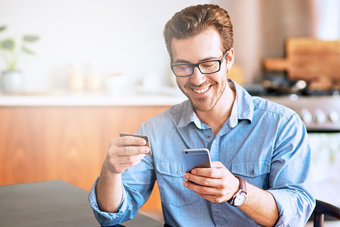 Young man using a cellphone and credit card at home