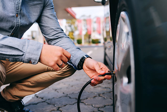 Man crouching on the gas station and inflating tire