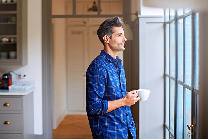 Young man drinking a coffee while looking through kitchen window