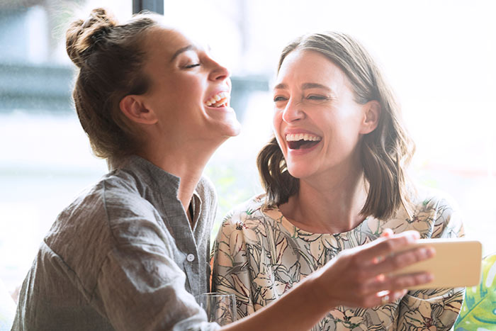 Woman holding mobile phone with friend laughing