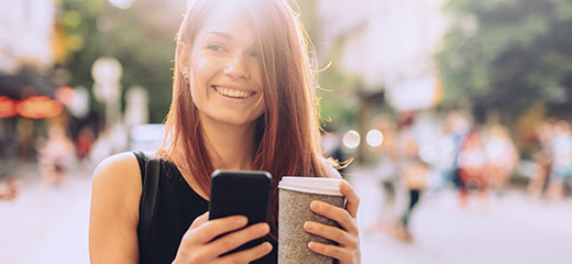 Young woman drinking coffee and texting outdoors