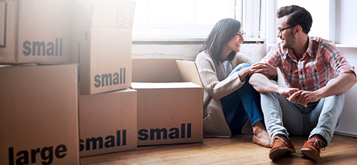 Couple sitting down on the floor, next to boxes.
