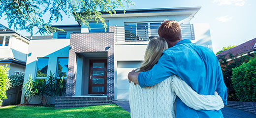 Couple hugging each other and looking towards a house.